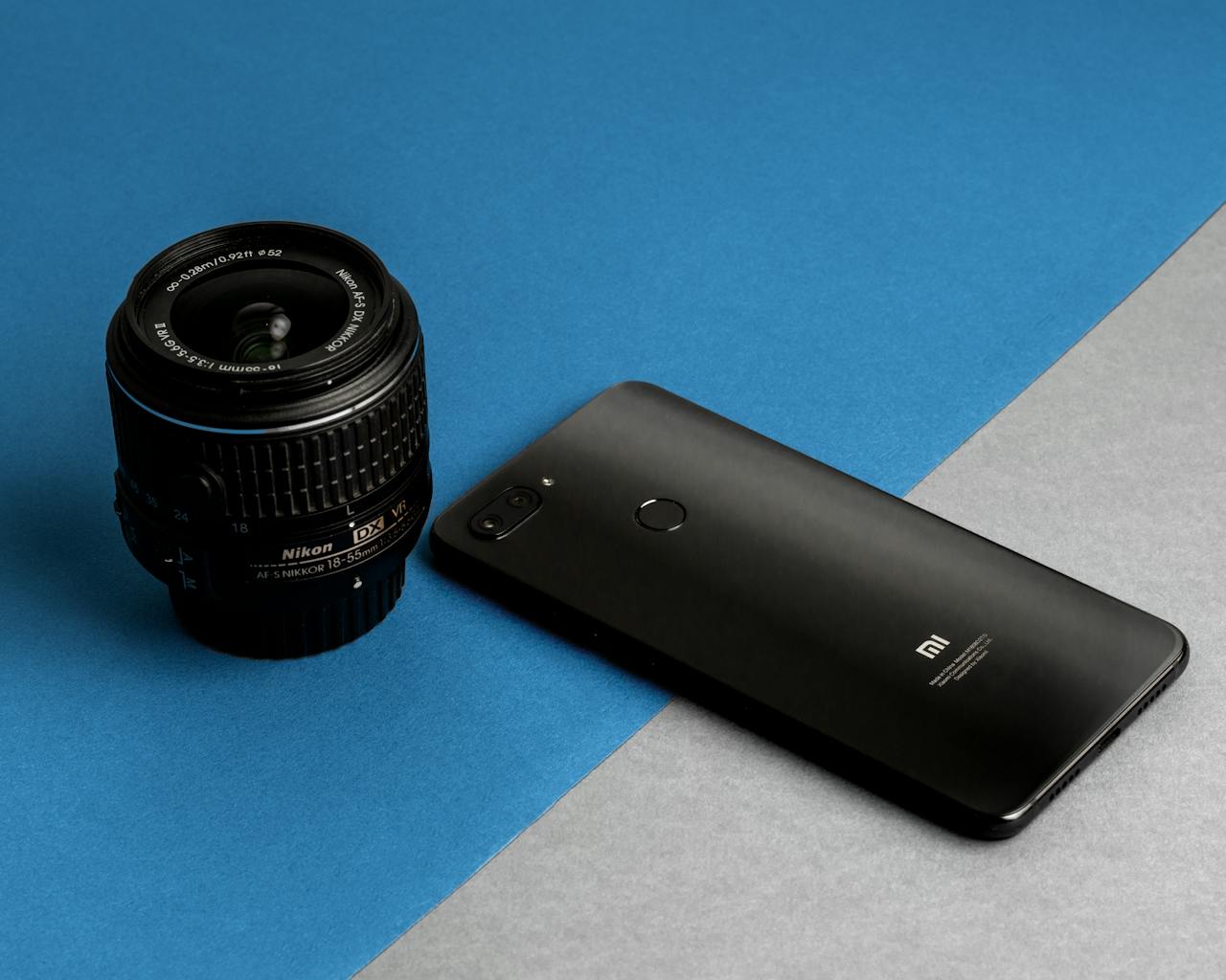 Close-up of a smartphone and camera lens on a blue and gray background.